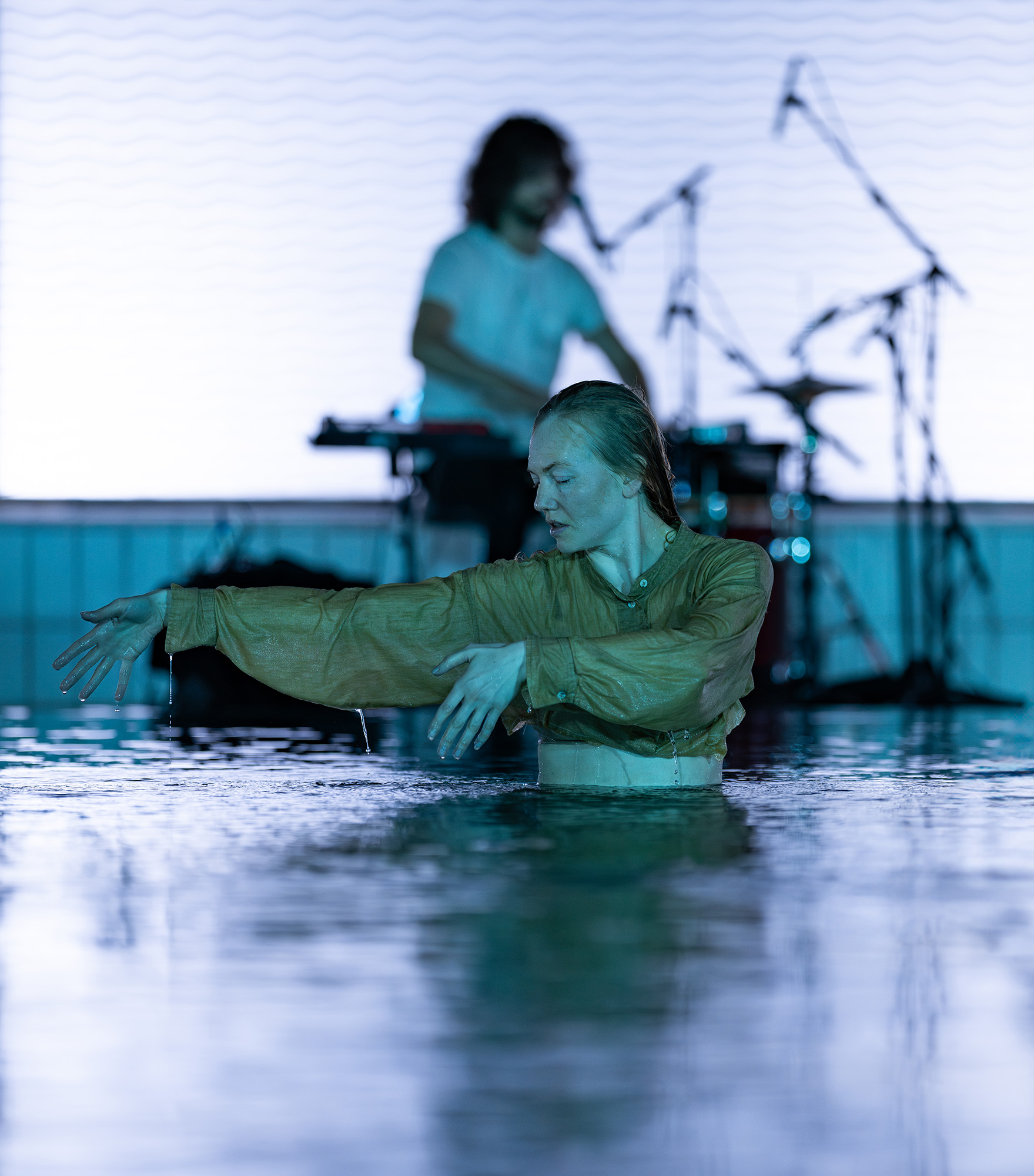Dancer in water with drummer in the background